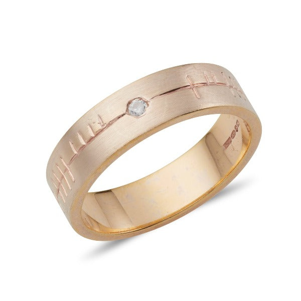18ct rose gold flat 6mm wide wedding ring with a matt finish and ogham engraving, there is a small diamond at the centre of the ring