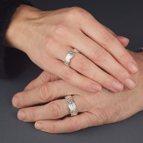 sterling silver celtic design matching his and hers rings, the pattern is embossed on the ring and the edges of the rings are wavy as shown on this womans and mans hands