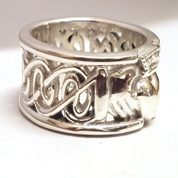 sterling silver 8mm wide calddagh band, there is a claddagh symbol in the centre of the ring with a pierced celtic design going around the ring, from the side view