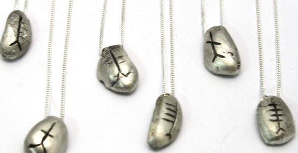 sterling silver pebble with chain going through the pendant, they are then engraved with an ogham initial